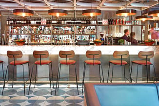 Moderne bar met houten barstoel in oranje en zwarte metalen poten, marmeren bartafel, verlichte glazen flessen achter bar, ha