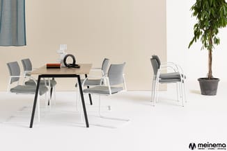 Kantoorinrichting met lichte tafel, witte stoelen met grijze bekleding, potplant en decoratieve objecten tegen beige wand.