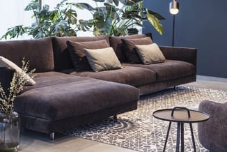 Bruine loungebank met chaise longue, decoratieve kussens, geplaatst in moderne kantoorruimte met grijs accent muur, potplante