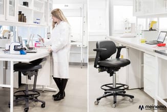 Twee zwarte werkstatekrukken met armleuningen en voetsteun in modern laboratorium met witte kasten en werkbladen.
