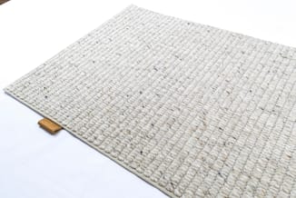 Crèmekleurig woven tapijt met ribbelpatroon en houten rand, schuin gefotografeerd op witte achtergrond.