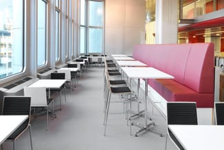 Modern kantoor met witte tafels, zwarte ergonomische stoelen, roze geluidswerend scherm en grote ramen met uitzicht op de sta