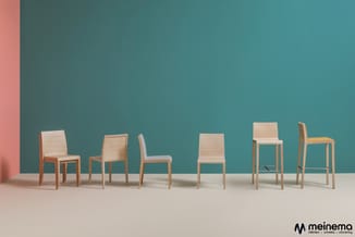 Zes houten stoelen in verschillende uitvoeringen tegen turquoise muur, op beige vloer. Meinemo logo rechtonder.