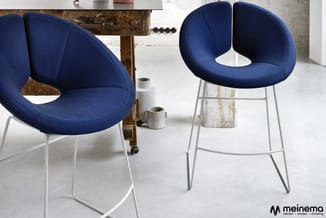 Blauwe designstoelen met witte metalen poten in industrieel interieur. Links stoel op wieltjes, rechts barkruk. Meinemo-logo