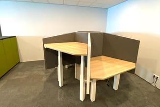Twee werkplekken met grijs akoestisch schermen, houten werkbladen en witte metalen poten in kantoorruimte met beige muren.