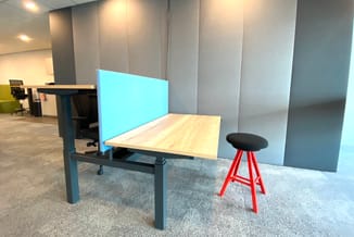 Werkplek met blauwe akoestische scherm, houten bureaublad, zwarte onderstel, rode kruk en grijze akoestische wandpanelen in k