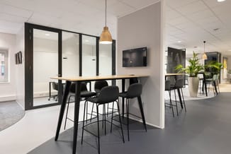 Moderne kantoorinrichting met zwarte bartafel, zwarte barkrukken, glazen vergaderbox met zwarte frames, wandmonteerde TV, han