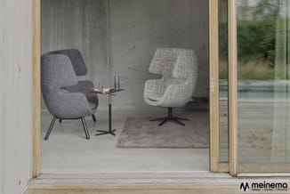 Twee gestoffeerde fauteuils met grijs/beige textiel en metalen poten in een minimalistisch interieur met betonnen wand, klein