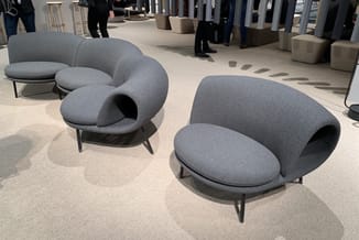 Grijze loungestoelen met organische vormen en metalen poten in showroomopstelling op lichte vloer.