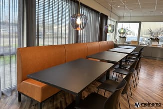 Moderne vergaderruimte met lange bruinleren banquetzitting, zwarte vergadertafels, zwarte stoelen, hangende glazen lampen en