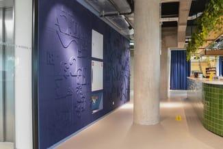 Moderne kantoorgang met donkerblauwe muurtegels met reliëf, betonnen zuil, groene plantenbak, gele vloermarkering en balie me