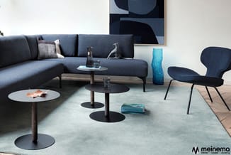 Grijsblauwe hoekbank met salontafels, blauwe fauteuil en abstracte wandkunst in moderne kantoorlounge.