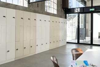 Rij cremekleurige kastenwanden met zwarte handgrepen in modern kantoor met betonnen plafond, glazen deuren en metalen stoelen