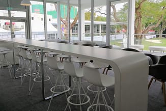 Moderne kantinetafel wit met zwarte barkrukken in open ruimte met glazen wanden en uitzicht op park.
