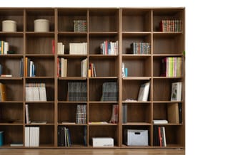 Houten boekenkast met zes kolommen en zes rijen vakken, gevuld met boeken, mappen en opbergdozen in bruintinterieur.
