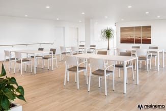 Modern kantoor met witte vergadertafels, witte stoelen met bruine zitting, houten vloer, witte wanden, plantendecoatie en bru