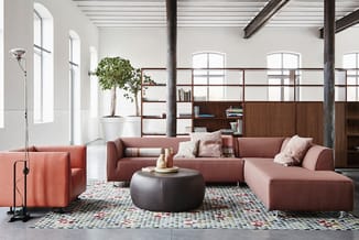 Moderne kantoorlounge met roze-bruin modulair bankstelsel, zwarte ronde poef, geometrisch tapijt, houten boekenkasten en grot