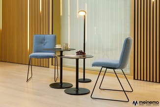 Moderne lounge met twee blauwe stoelen, zwarte bijzettafels, staanlamp en gouden verticale wandpanelen.