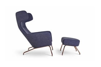 Donkerblauwe fauteuil met hoge rugkuil en bijbehorende voetenbankje, beide op koperen metalen poten, tegen witte achtergrond.