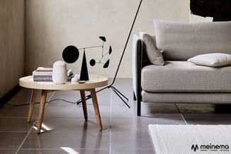 Minimalistisch ingerichte woonkamer met beige stof sofa, rond houten bijzettafeltje met decorobjecten, zwart statief en witte