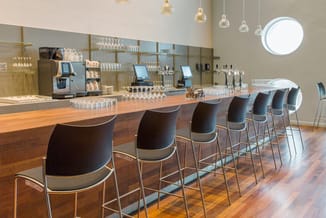 Moderne barruimte met houten balie, zwarte barkrukken met metalen frame, spiegelwand, hangende glazen lampen en POS-terminals