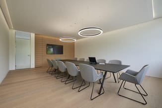 Modern vergaderruimte met zwarte tafel, grijze standen stoelen, houten wandafwerking, LED-verlichting en TV-scherm.