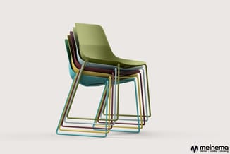 Gestapelde kleurrijke kantinestoelen met kunststof zitting en metalen buisframe in groen, blauw, bordeaux en geel tegen licht