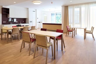 Modern kantoor met houten eettafels, houten stoelen met rode en gele zittingen, witte keukenkast, donkerbruine backsplash, gr