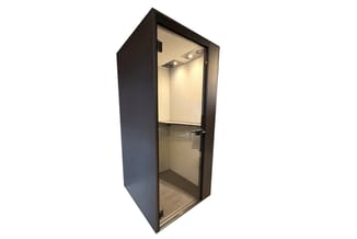 Zwarte belcel met glazen deur, ingebouwde verlichting en grijze vloer voor kantoorruimte.