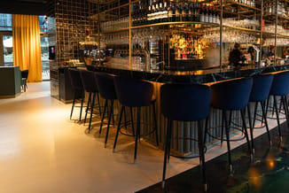 Moderne bar met zwarte barkrukken, zwart marmeren bartafel en gouden details. Achtergrond met verlichte flessen en glaasjes t