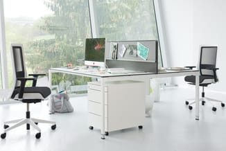 Modern kantoorinterieur met wit bureau, zwarte ergonomische stoelen, witte kasten met wielen en grote ramen met bosouitzicht.
