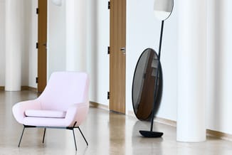 Roze fauteuil met zwart metalen poten en zwarte staande spiegel in moderne kantoorruimte met witte kolommen en houten deuren.