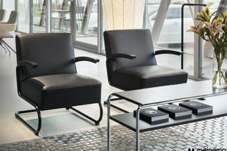 Twee zwarte leren fauteuils met metalen frame rond een witte tafel in moderne kantoorruimte met glazen wanden.