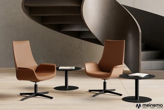 Twee cognackleurige leren loungefauteuils met zwart onderstel rond kleine zwarte tafel in moderne kantoorruimte met grijze wa