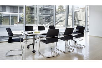 Moderne vergaderruimte met zwarte netkatoenen stoelen op wielen en vaste poten, rond een zwarte tafel met glazen blad, grote