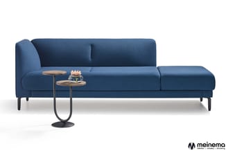 Blauwe loungebank met chaise longue, zwarte poten, toegesteld met houten bijzettafel en decoratieve objecten tegen witte acht