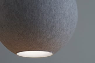 Hangende textiellampen met grijs stofoppervlak en verlicht onderpaneel tegen neutrale wand.
