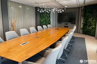 Moderne vergaderruimte met lange houten tafel, grijze ergonomische stoelen, groene plantenwanden, hangende design lamp en gro