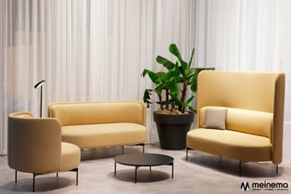 Moderne lounge-opstelling met gele stoffen zitmeubels, zwart bijzettafeltje, plant in pot en staande lamp tegen witte gordijn