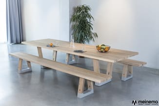 Houten vergadertafel met witte ondersteuning en twee bijpassende lange zitbanken in heldere ruimte met plant.