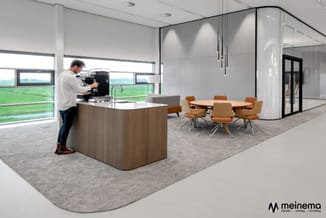 Modern kantoor met houten keukenblok, witte glazen wanden, ronde houten vergadertafel met cognackleurige stoelen en uitzicht