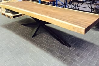 Houten vergadertafel met natuurlijke afwerking op zwart stalen kruisonderstel, in showroomruimte op tegelvloer.