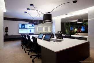 Modern kantoor met witte vergadertafel, zwarte bureaustoelen, zwarte hangende lampen, werkstations met monitoren en witte wan