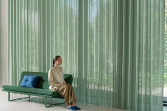 Groen zitbank met blauwe kussens in minimalistische ruimte met groene verticale lamellen en witte wanden.