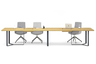 Lange houten bureau met zwart metalen onderstel en drie grijze bureaukstoelen met wieltjes. Laptop en kantoorspullen op het b