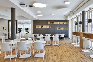 Modern kantoor met witte stoelen rond ronde tafels, grijze akoestische wandpanelen met houten inbouwkasten, houten vloer, han