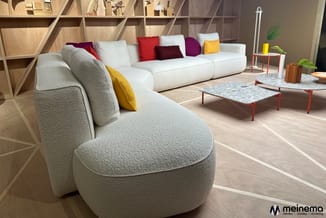 Moderne woonkamer met creme kleurige ronde fauteuil vooraan, lang wit modulair zitmeubel met gekleurde kussens, houten wandka