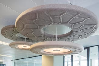 Hangende akoestische plafondpanelen in grijsbruin vilt met bladmotief en geïntegreerde verlichting in modern kantoor.