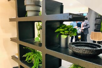 Modulaire wandkast met zwarte vakken en houten frame, beplant met groene planten en decoratieve objecten in kantooromgeving.