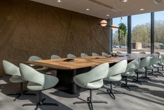 Moderne vergaderzaal met houten vergadertafel, witte draaibare stoelen, grijze vloer, wanddecoratie met plattegrond, hangende